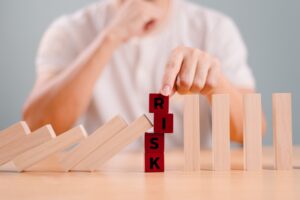 Hand stopping falling dominoes next to wooden block with the word risk, symbolizing crisis prevention, financial analysis, and real estate business risk management.